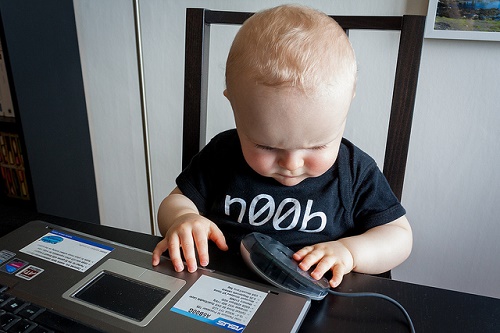 A baby sits at a keyboard studying intently a mouse \
	that is upside down